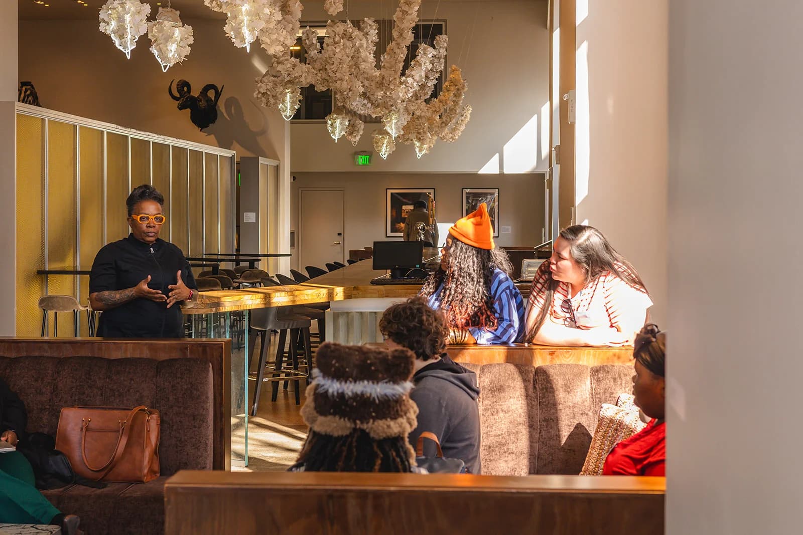 A speaker talks with community members gathered in a sunlit restaurant